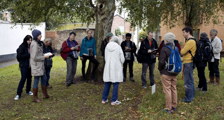 Group of Drama students outside writing notes, standing underneath a tree