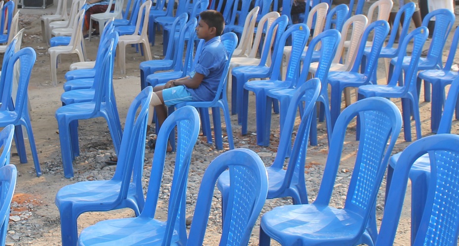 Boy dressed in blue, sitting on a blue chair in rows of blue chairs